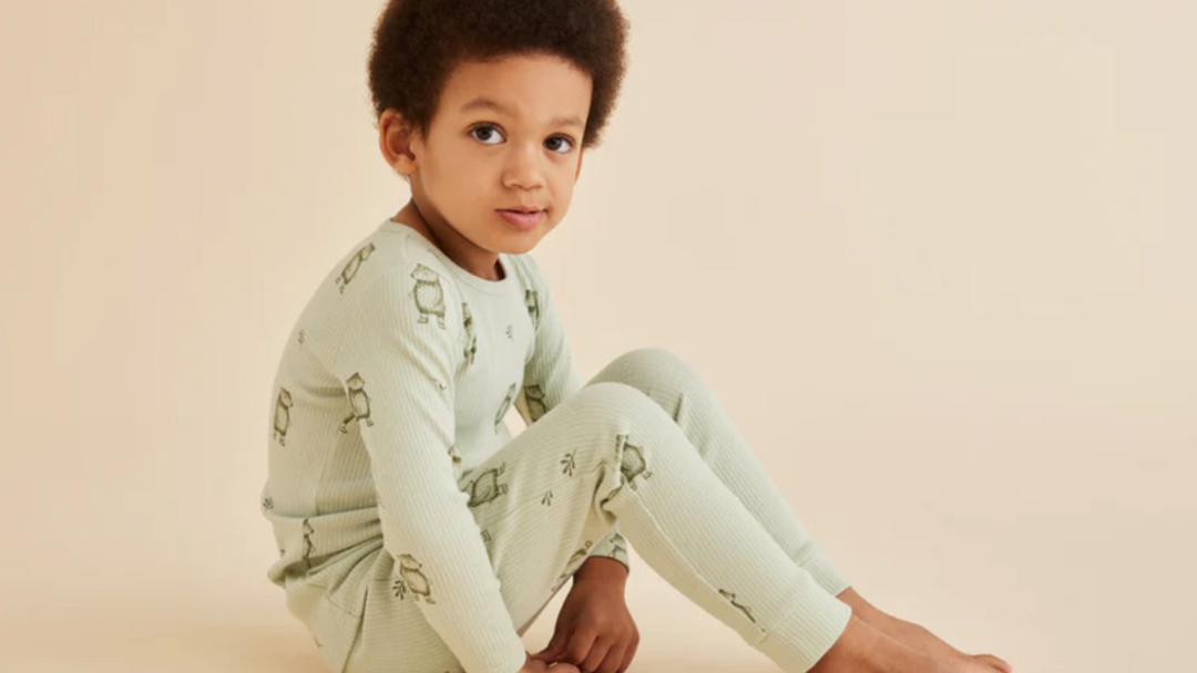 A young boy sitting on the floor in a green pajama set.