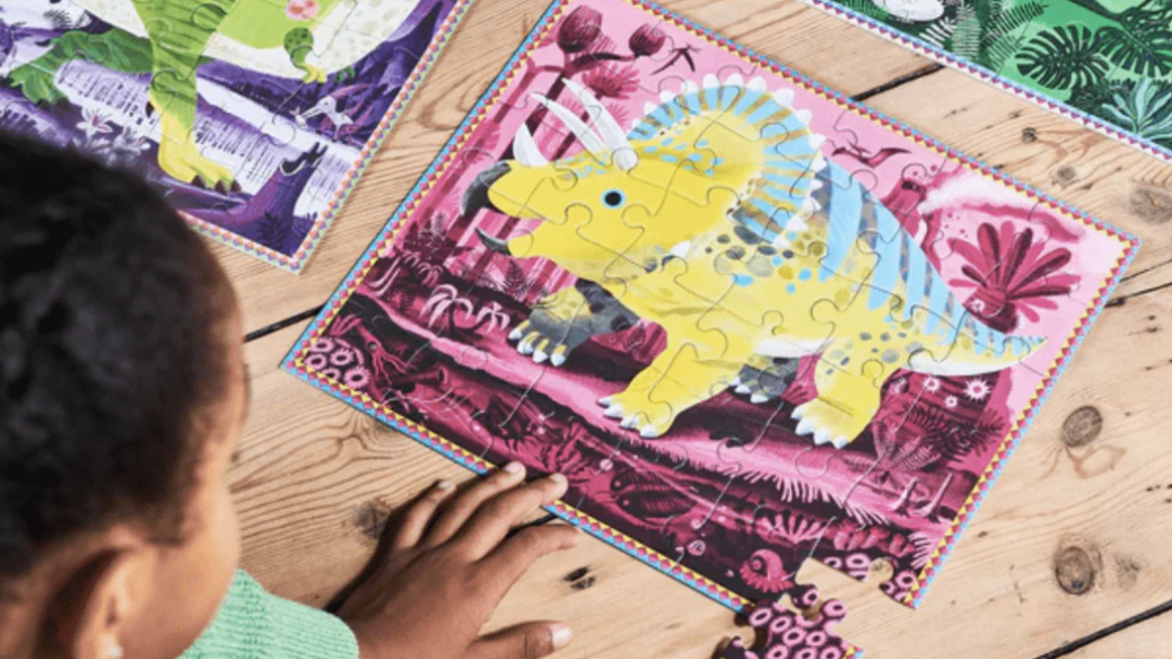 A child is playing with dinosaur puzzles on a wooden floor.