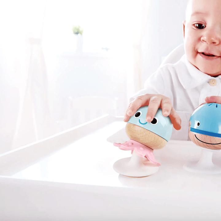 A baby in a Hape high chair playing with toys.