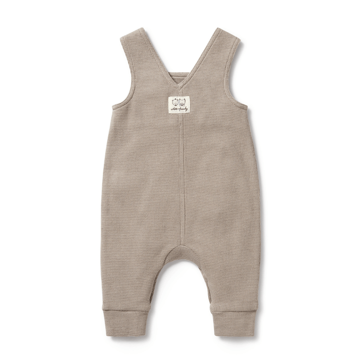 The beige sleeveless baby romper, now presented as the Wilson & Frenchy Organic Waffle Overalls in Brilliant Blue, is made from GOTS-certified organic cotton and features a small white patch on the chest with a logo of two animals and text. Designed with ribbed fabric and leg openings, these organic waffle overalls ensure both comfort and eco-friendliness for children aged 18-24 months.