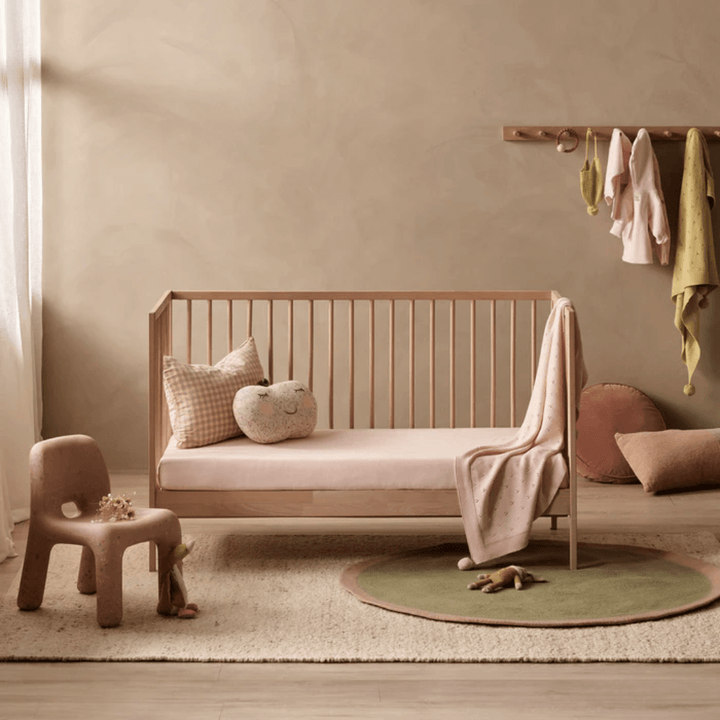 Cozy children's room with a Wilson & Frenchy Organic Rib Cot Sheet, soft textiles made of organic cotton, and a circular green rug.