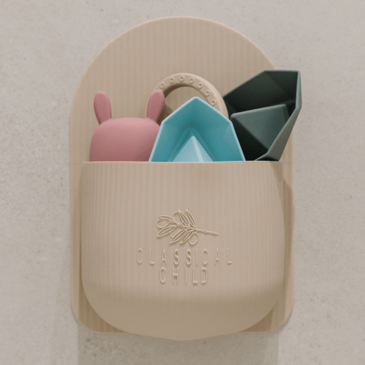 The "Classical Child Silicone Bath Toy Caddy - LUCKY LASTS" wall-mounted organizer in beige features a BPA-free silicone design that gracefully holds a pink bunny toy along with geometric shapes in calming pastel colors.