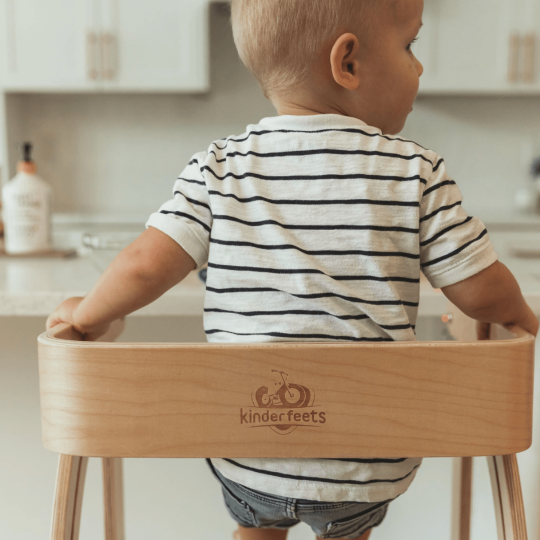 A baby sits in a Kinderfeets Pikler Observation Tower, engaging in imaginative play in the kitchen.