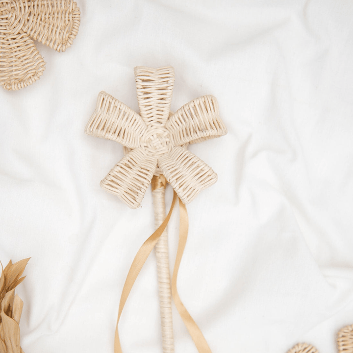 The Woodlands' Classical Child Rattan Flower Wand - LUCKY LASTS, ideal for imaginative play, showcases beige ribbons gracefully laying against a white fabric backdrop.