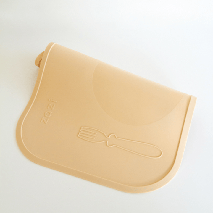 The Zazi Clever Mat is a beige, food-grade silicone placemat with the brand name 'Zazi' embossed on the left side and a fork outline on the right. It features advanced suction technology to keep it firmly in place and is rolled slightly at the top.