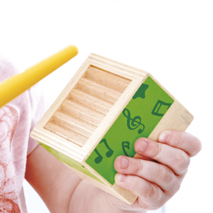 A child is holding a wooden box with a yellow drumstick from the Hape Stacking Music Set by Hape.