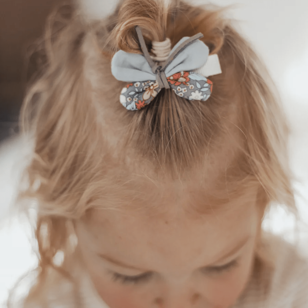 A child's hair is styled with a floral and blue bow hair tie, complemented by the Over the Dandelions Butterfly Hair Clips - LUCKY LAST.