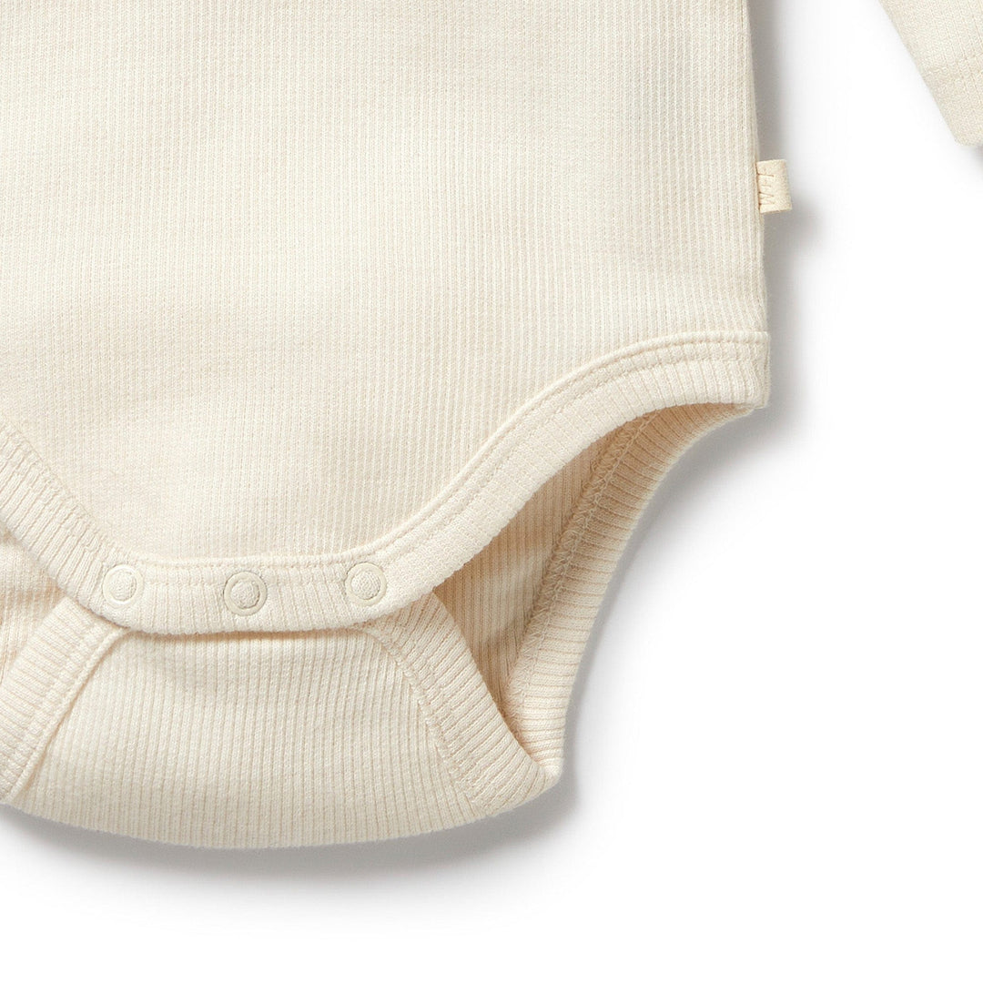 Close-up of the Wilson & Frenchy Organic Rib Long Sleeved Onesie in fawn, GOTS-certified organic cotton with snap buttons at the bottom and a small fabric tag on the side seam.