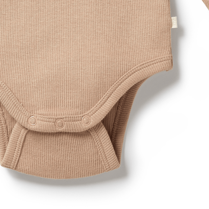 Close-up of a beige ribbed Wilson & Frenchy Organic Rib Long Sleeved Onesie, showcasing the bottom half with snap buttons. This essential piece from the baby wardrobe is made from soft, organic cotton rib.