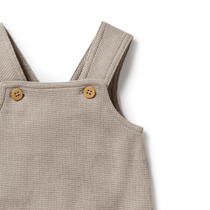 The Brilliant Blue, sleeveless Wilson & Frenchy Organic Waffle Overalls, available only in size 18-24 months, are made from GOTS-certified organic cotton and feature a ribbed texture with two charming wooden buttons on the straps.