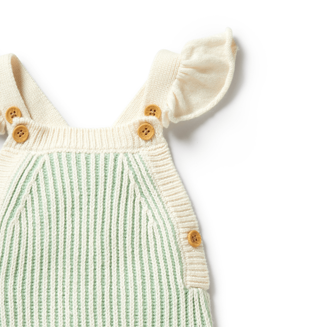 Wilson & Frenchy's Knitted Ruffle Overalls in Dijon features charming green and white stripes, wooden button details on the shoulders, and delightful ruffled shoulder straps.