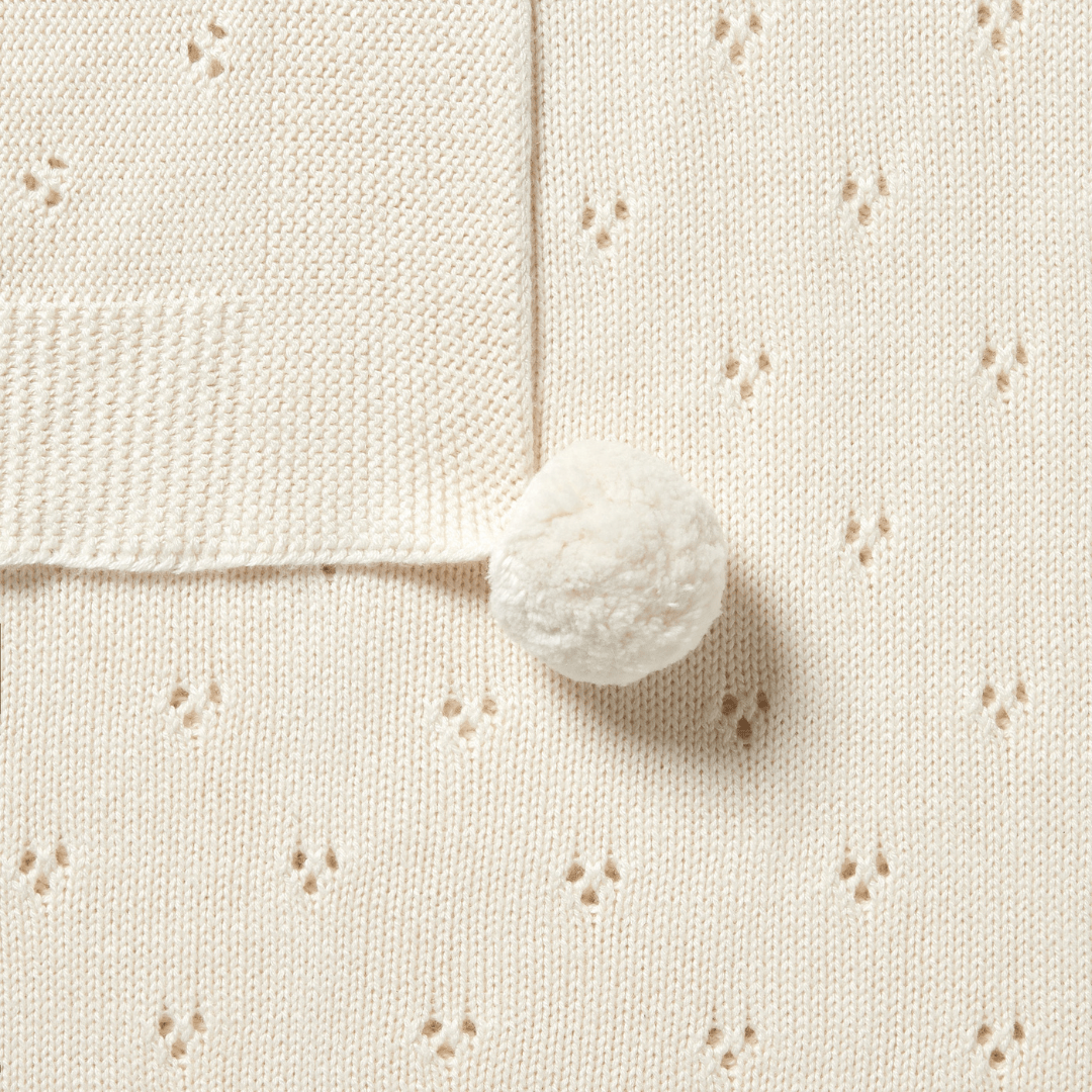 Close-up of a mint green knitted fabric with a small polka-dot pattern and a fluffy pom-pom, perfect as an heirloom design baby shower gift. Wilson & Frenchy Knitted Pointelle Baby Blanket - LUCKY LASTS.