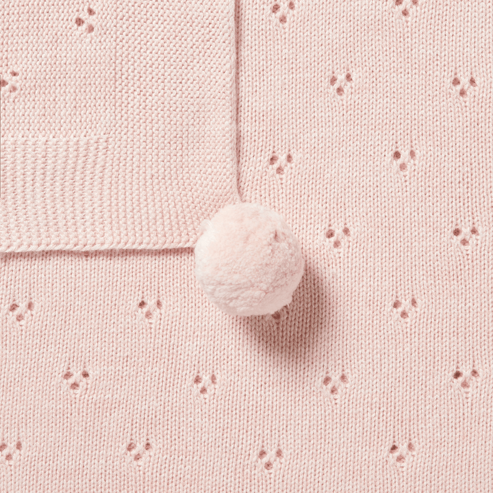 Close-up of a mint green knitted fabric with small holes in a subtle pattern and a single fluffy pom-pom attached, making the Wilson & Frenchy Knitted Pointelle Baby Blanket an ideal cherished baby shower gift.