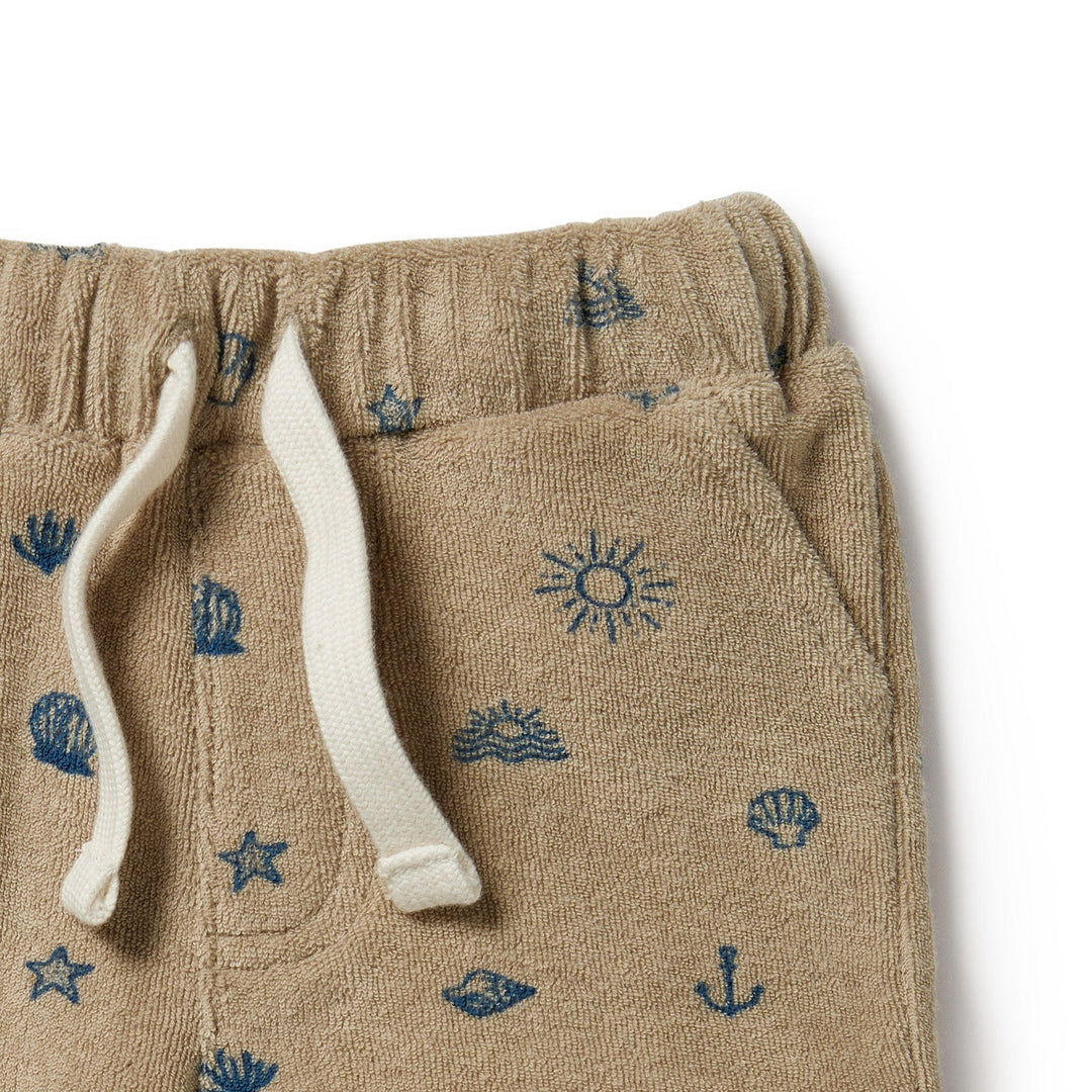 Close-up of Wilson & Frenchy Organic Terry Shorts - LUCKY LASTS - 0-3 MONTHS ONLY in beige, featuring an elastic waist with white drawstrings and blue nautical-themed patterns such as anchors, seashells, and stars. Made from GOTS-certified organic cotton, these shorts are the ultimate summer staple.