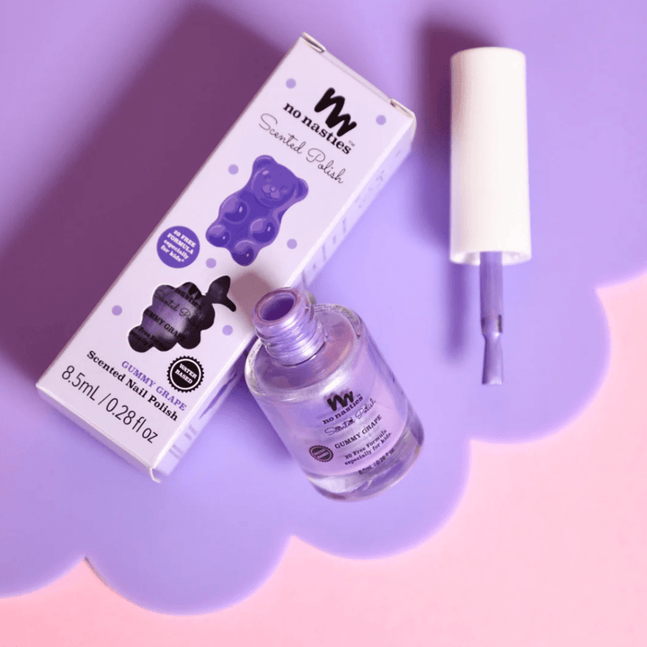 A bottle of No Nasties 20 FREE Kids Scented Nail Polish in a purple hue, complete with its box and brush applicator, set against a purple and pink background. The box displays a bear illustration and product details, making it an ideal choice for children's nail polish.