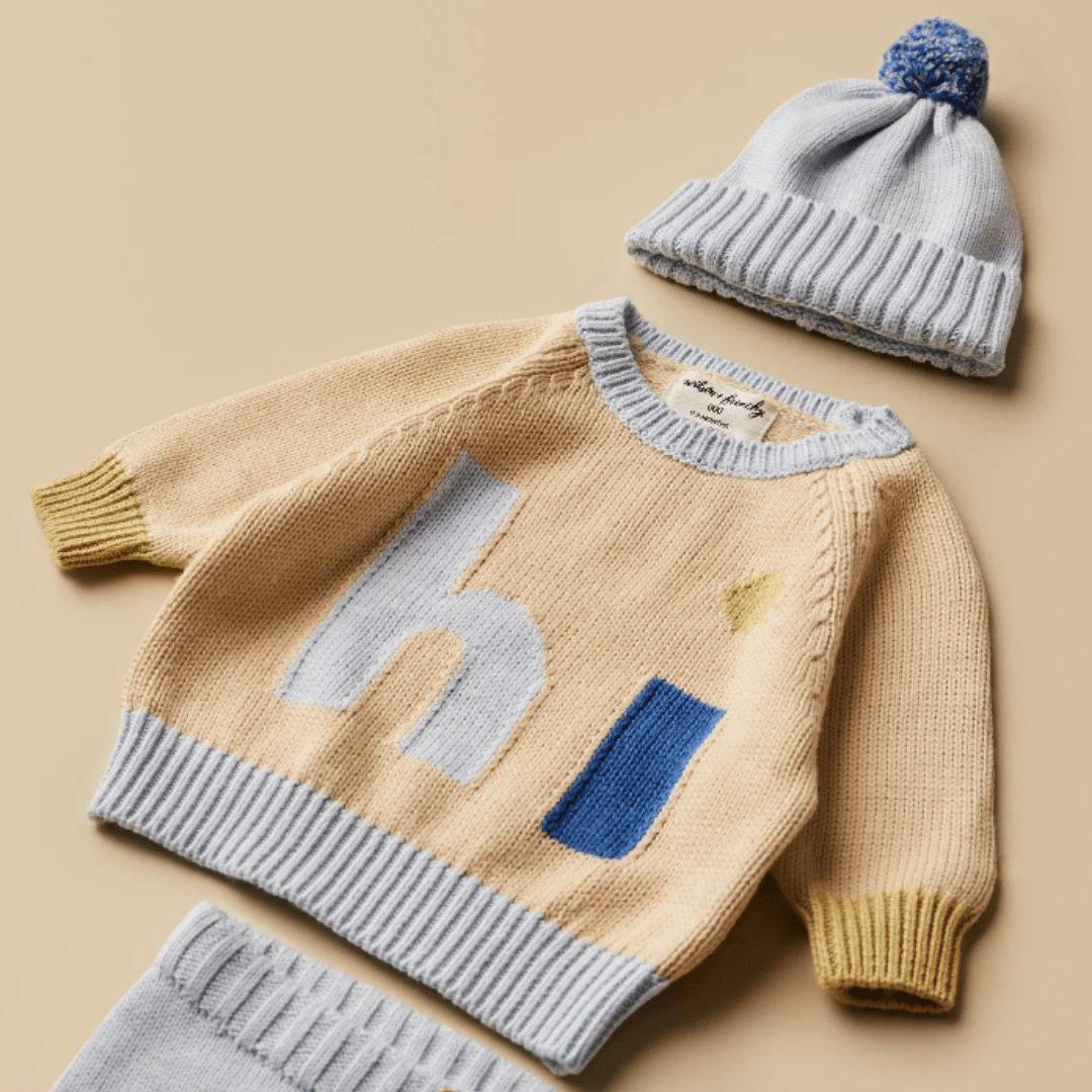 A baby's outfit consisting of a Wilson & Frenchy Knitted Jacquard Jumper and matching hat on a beige background.