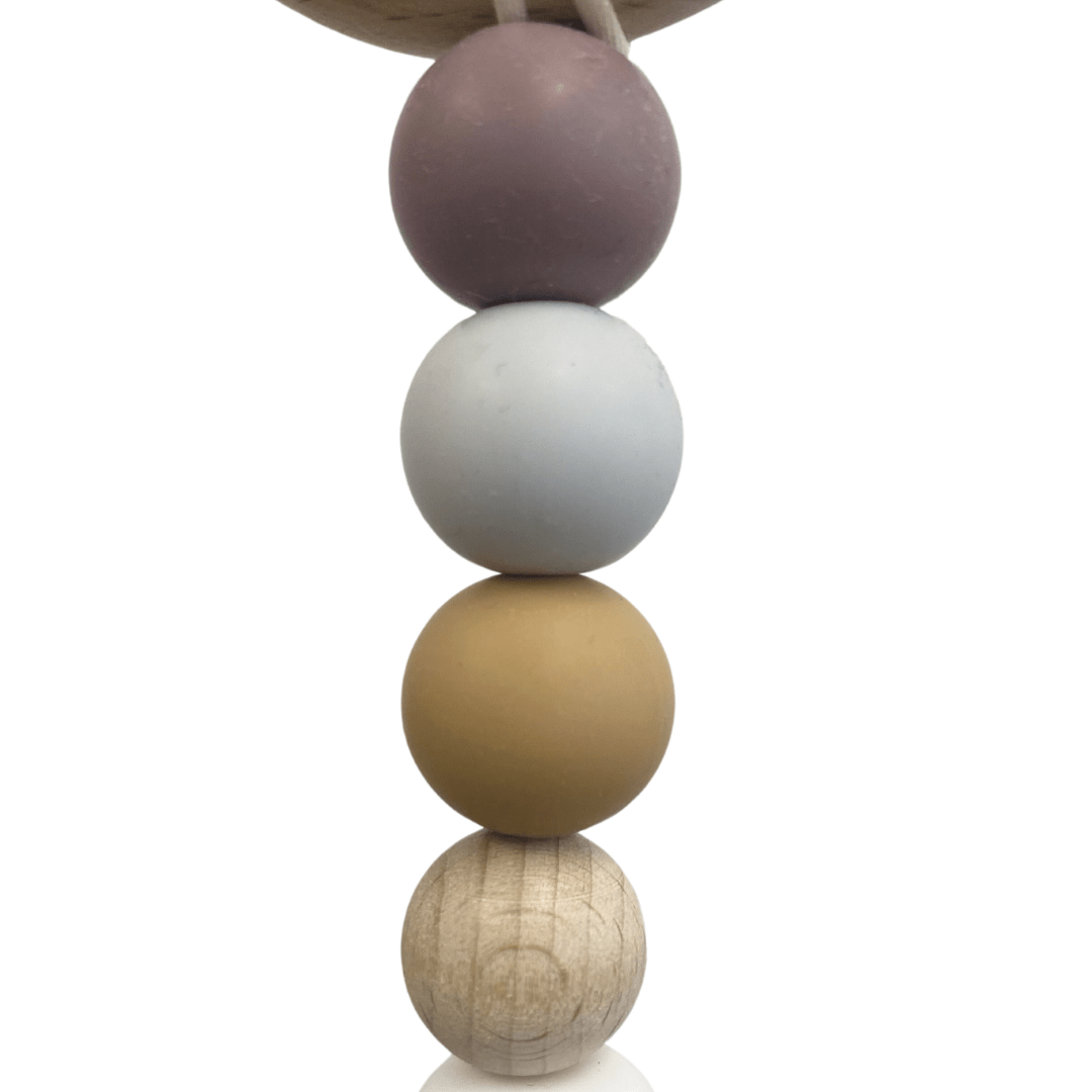 The Funny Bunny Kids Silicone & Beechwood Pram Garland features an enchanting vertical arrangement of four spheres in assorted colors: purple, light blue, tan, and wood texture. Meticulously crafted by Funny Bunny Kids, this delightful baby toy seamlessly combines playful silicone beads with a whimsical flair.