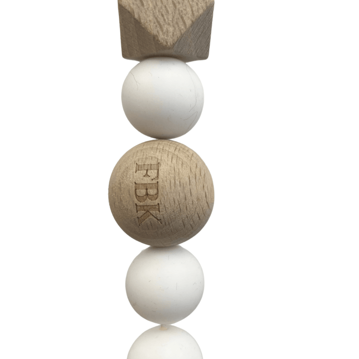 Close-up of the Funny Bunny Kids Silicone & Beechwood Pram Garland, ideal as a decorative pram accessory or baby toy. It showcases alternating white silicone and natural beechwood beads, with added texture from the silicone. The central wooden bead is engraved with "FBK.