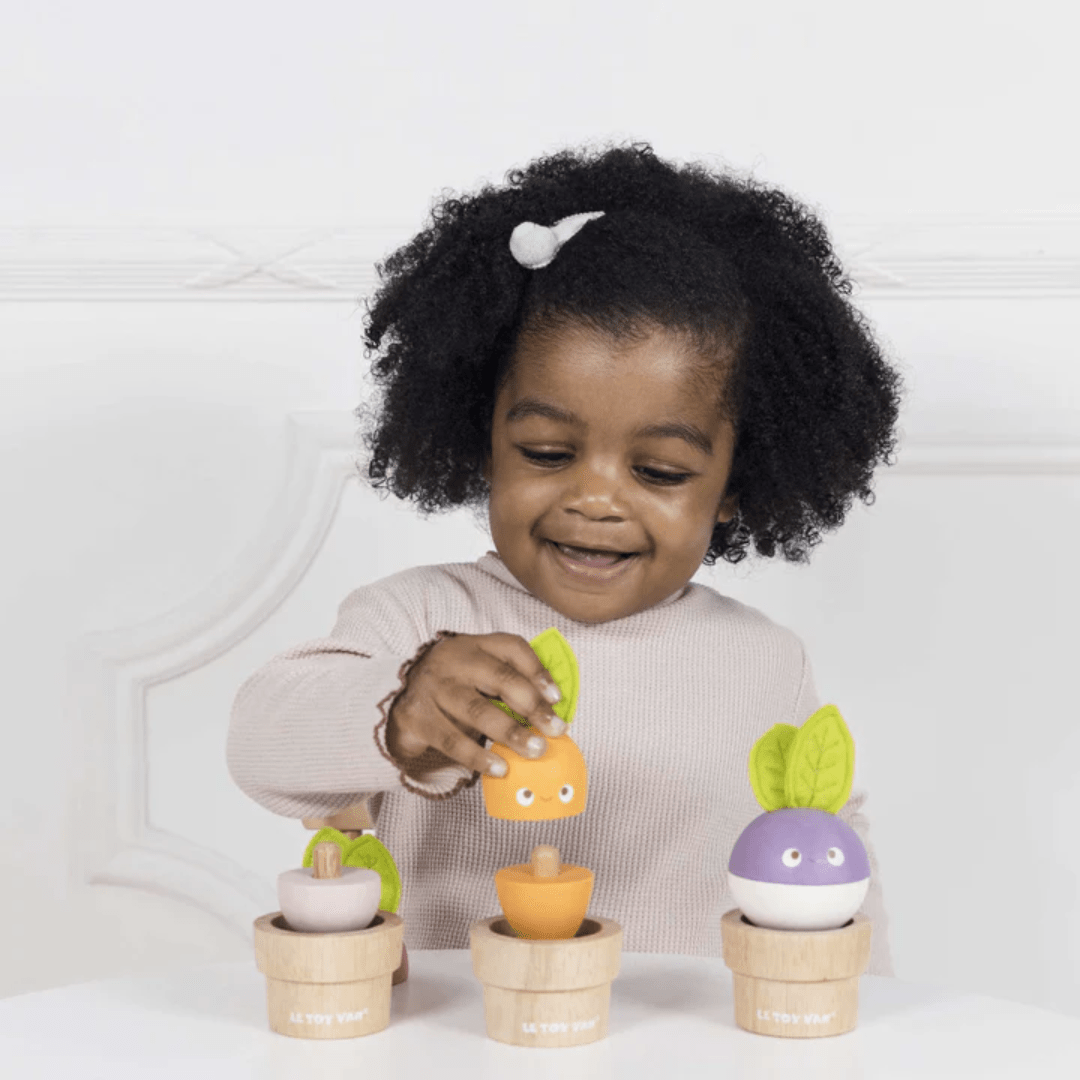 A child beams with joy, using fine motor skills to place an orange vegetable into the center of a beautifully crafted sustainable wood pot, as part of the charming Le Toy Van Stacking Veggies - LUCKY LAST wooden toy set.