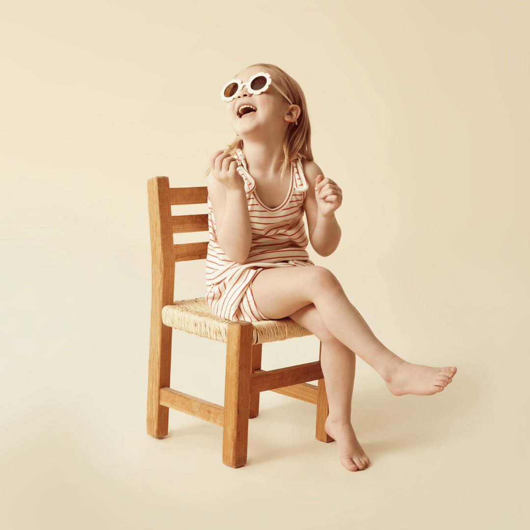 A little girl wearing sunglasses sitting on a wooden chair wearing Wilson & Frenchy Organic Rib Stripe Kids Bloomer Shorts (Multiple Variants) made from GOTS-certified organic cotton by Wilson & Frenchy.