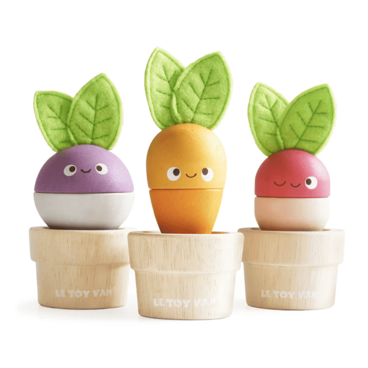 The Le Toy Van Stacking Veggies - LUCKY LAST set features a charming trio of smiling wooden toy vegetables in pots, each adorned with green leafy tops. It includes a purple turnip, a yellow carrot, and a red radish. Crafted from sustainable wood by Le Toy Van, this delightful set also functions as a stacking toy designed to enhance fine motor skills.