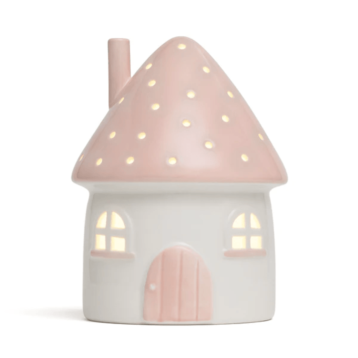 The Little Belle Nightlights Ceramic Nightlight - LUCKY LASTS - FAIRY HOUSE ONLY is a whimsical charm from Little Belle Nightlights, crafted from porcelain. This small, house-shaped nightlight features a white design with a pink roof and circular cutouts, allowing warm light to emit through the windows and roof openings.