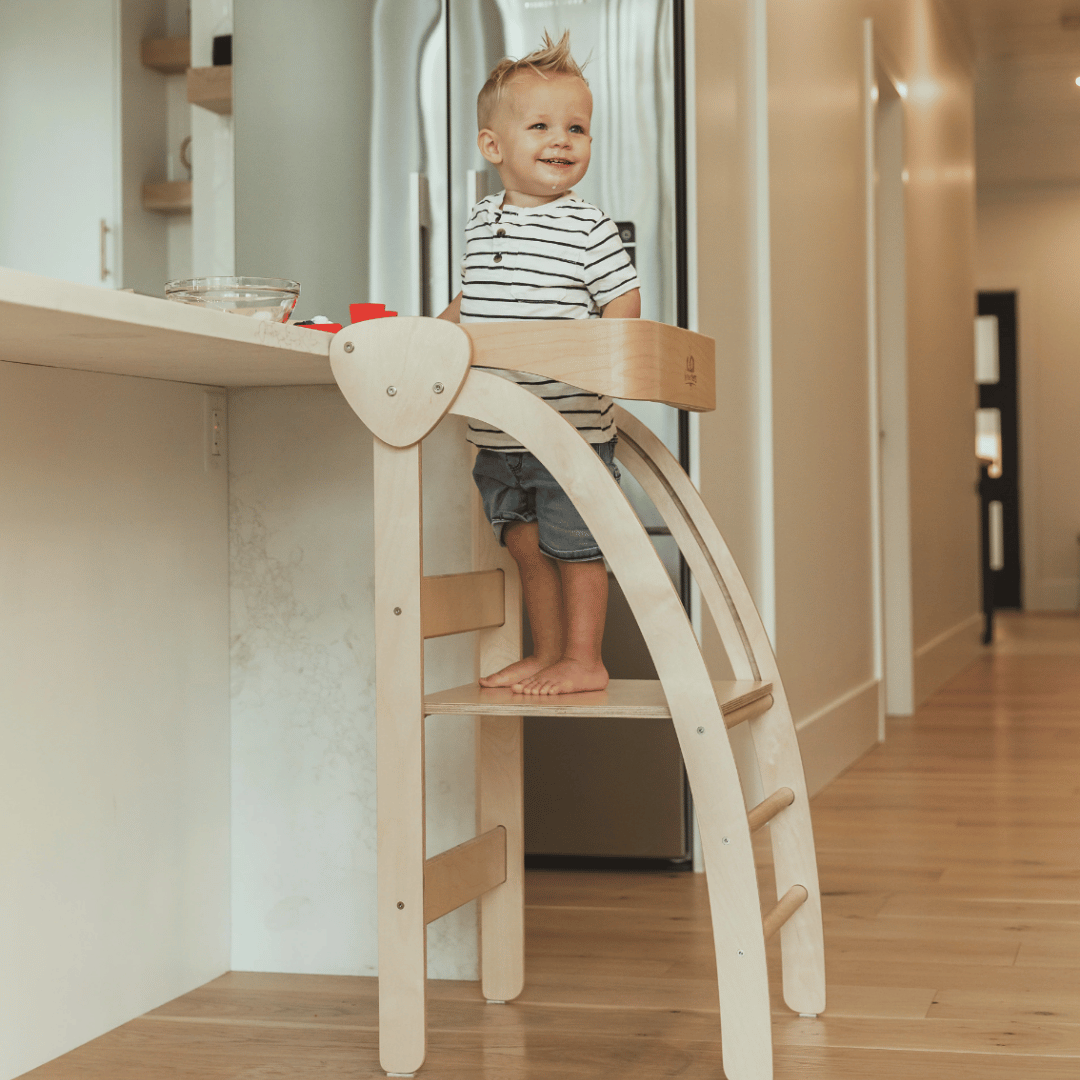 A child stands on the Kinderfeets Pikler Observation Tower, engaging in imaginative and functional play in a kitchen.