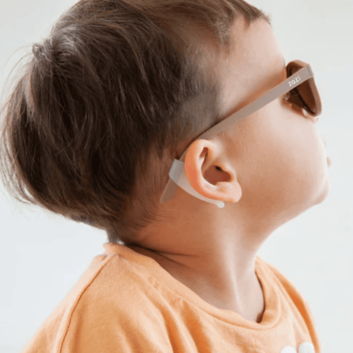 A young child wearing Zazi Ear Grips and an orange shirt looks upward.