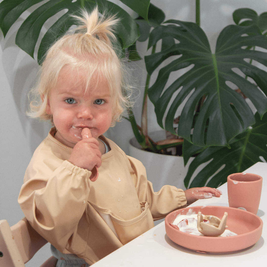 A little girl sitting at a table with a Zazi Recycled Full-Sleeved Bib (Multiple Variants).