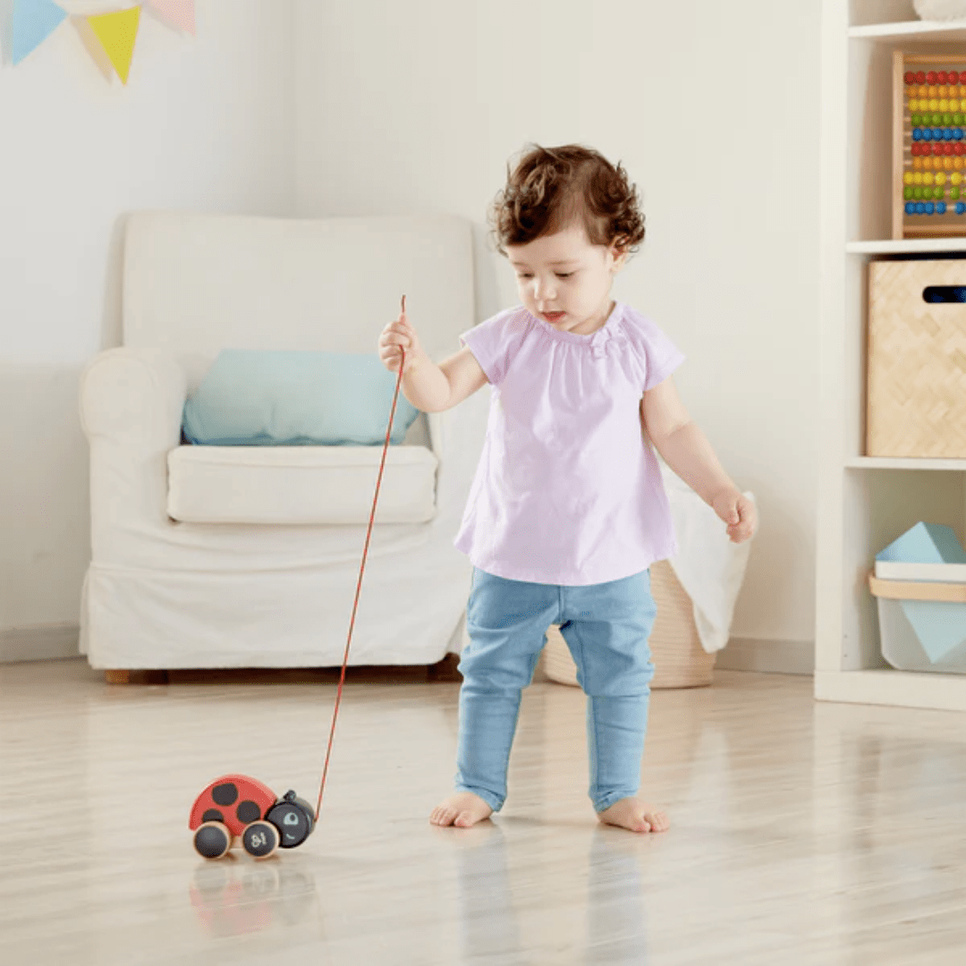 Little-Girl-Playing-With-Hape-Pull-Along-Toy-Ladybug-Naked-Baby-Eco-Boutique