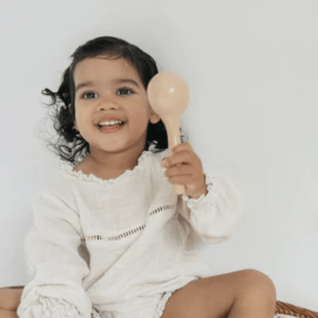 Little-Girl-Playing-With-Over-The-Dandelions-Wooden-Maraca-Naked-Baby-Eco-Boutique