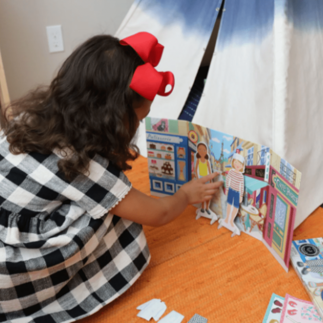 A little girl engaged in imaginative play with an eeBoo Paper Doll Set on the floor.