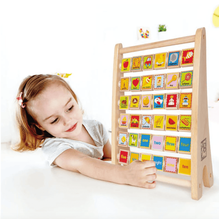 A child engages with the Hape Alphabet Abacus featuring colorful tiles displaying ABC and numbers, shapes, and images, set up on a table in a bright indoor environment.