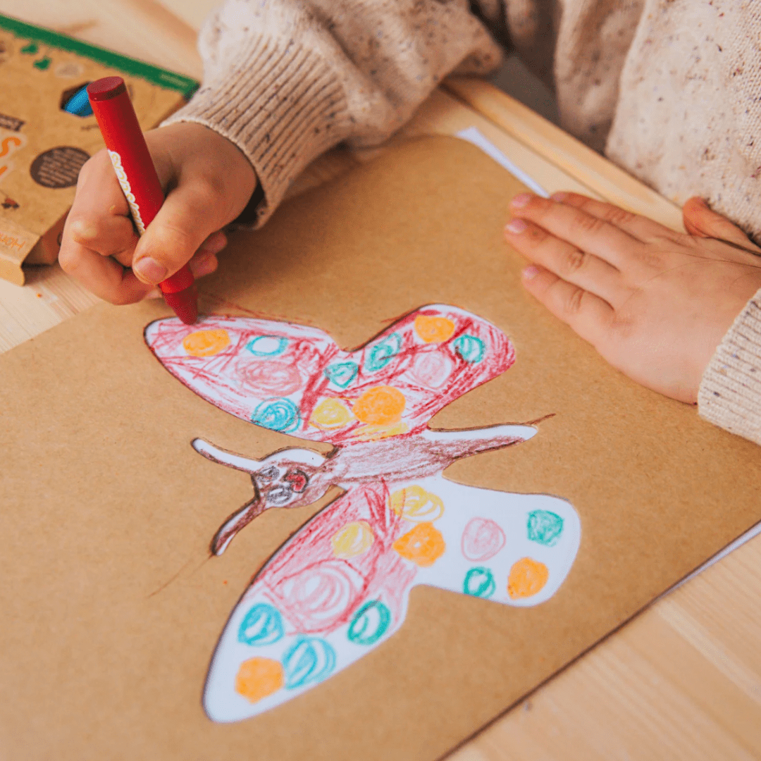 A child coloring a butterfly drawing with markers on a brown sheet of paper from the Honeysticks Jumbo Stencil & Crayon Activity Set by Honeysticks.