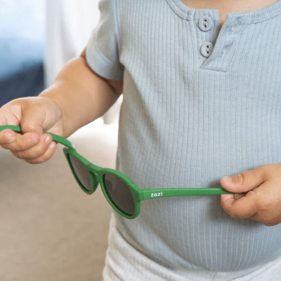 A young boy holding a pair of Zazi Shades Baby & Toddler Sunglasses with polarized clarity.