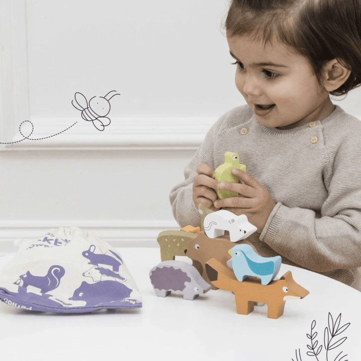 A little girl is playing with a Le Toy Van Wooden Stacker Tower and Bag, improving her dexterity skills.