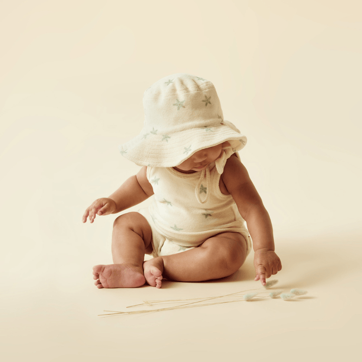 A baby wearing a Wilson & Frenchy Organic Terry Tie Singlet (Multiple Variants) and playing with sticks.