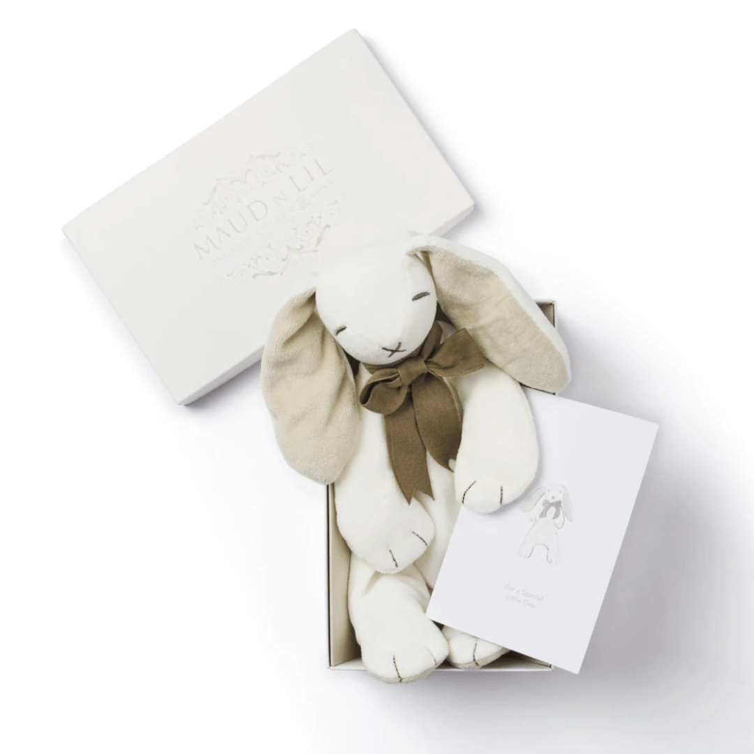 Displayed in an open box with a card, the Maud N Lil Organic Bunny Comforter features a charming white stuffed rabbit with beige ears and a brown bow. Branded as "Maud N Lil," this delightful organic cotton toy makes an ideal baby gift.