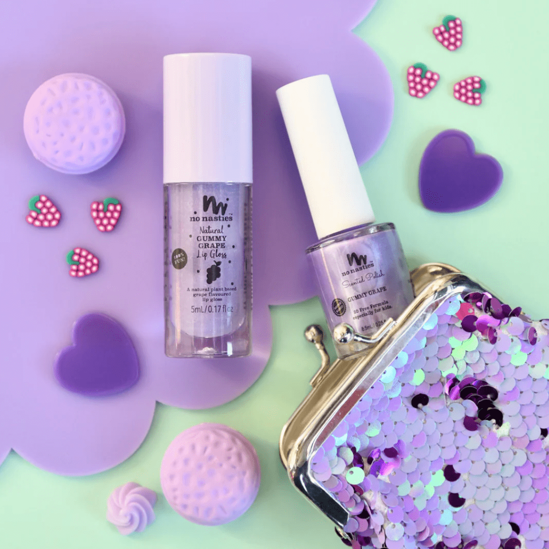 Two bottles of No Nasties 20 FREE Kids Scented Nail Polish, a sequined purple coin purse, and several small purple and pink decorations are arranged on a mint green background.