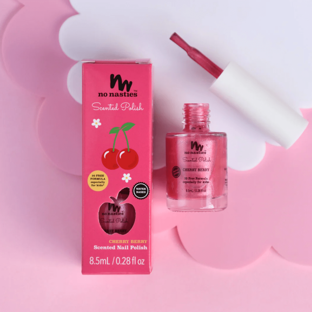 A pink bottle of "No Nasties 20 FREE Kids Scented Nail Polish" labeled "Cherry Berry" sits next to its box. A brush leans on the bottle, showcasing the polish color. The backdrop features pink scalloped edges.