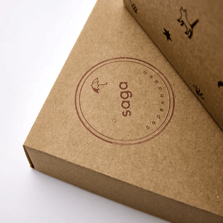 The Saga Copenhagen Gift Box - Elina is encased in brown packaging adorned with small decorative icons, including a bird and stars. Made from eco-friendly materials, it exemplifies Saga Copenhagen's dedication to sustainability.