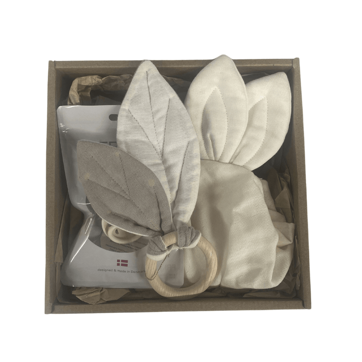 The Saga Copenhagen Gift Box - Elina includes a pacifier, a wooden ring adorned with fabric leaves, and a charming bonnet with rabbit ears, each made from organic cotton. This enchanting set is thoughtfully packaged in eco-friendly materials.