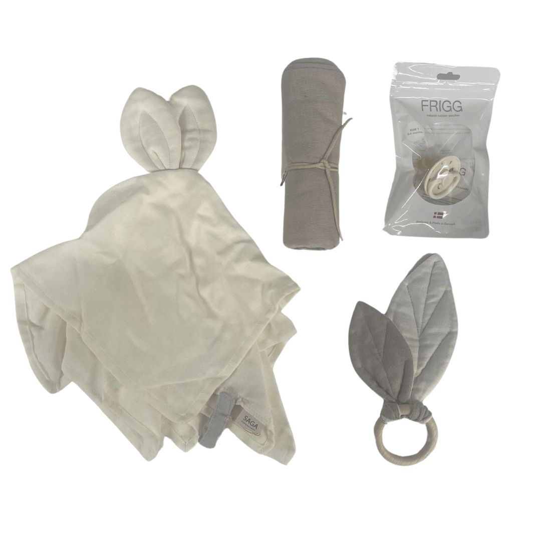 The Saga Copenhagen Gift Box - Elina by Saga Copenhagen contains charming baby essentials: a beige blanket with bunny ears, a gray cloth roll, an eco-friendly packaged pacifier, and a ring toy with gray fabric ears—all made from soft organic cotton.