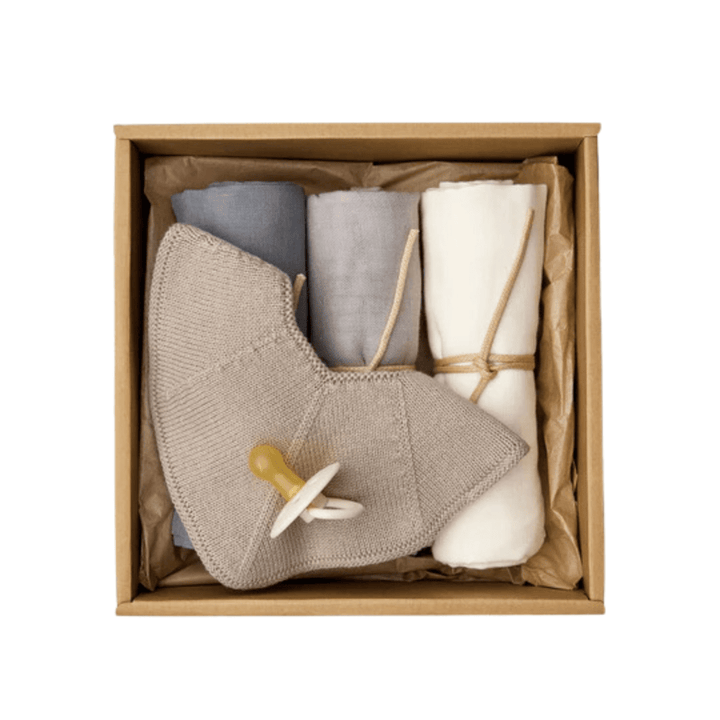 A neatly arranged Saga Copenhagen Snuggle-Up Gift Box from Saga Copenhagen containing a gray knit lovey with a pacifier, and three rolled cloths in blue, gray, and white, crafted from organic cotton baby products.