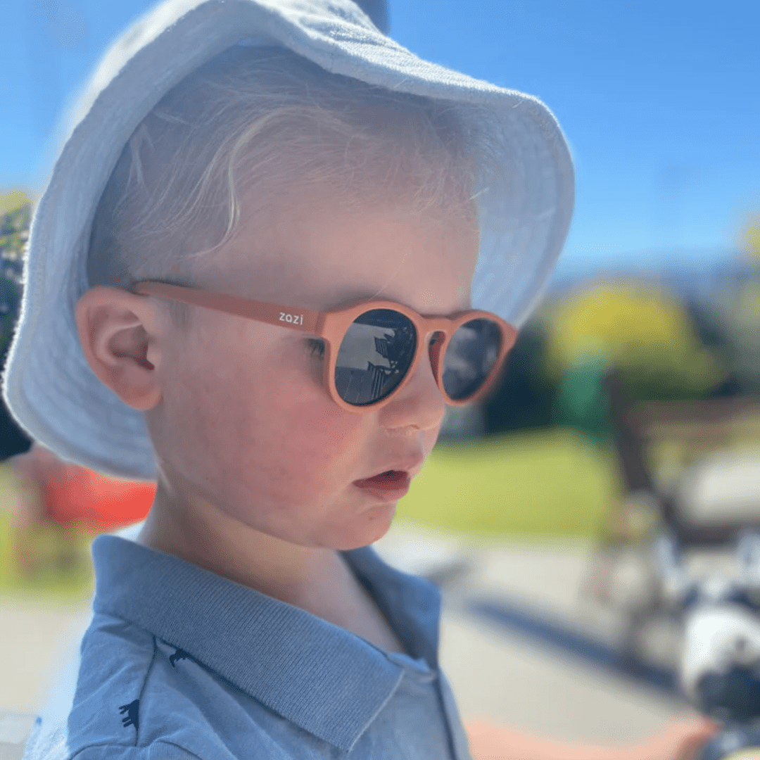 A young boy wearing Zazi Shades Baby & Toddler Sunglasses and a hat with UV400 protection.