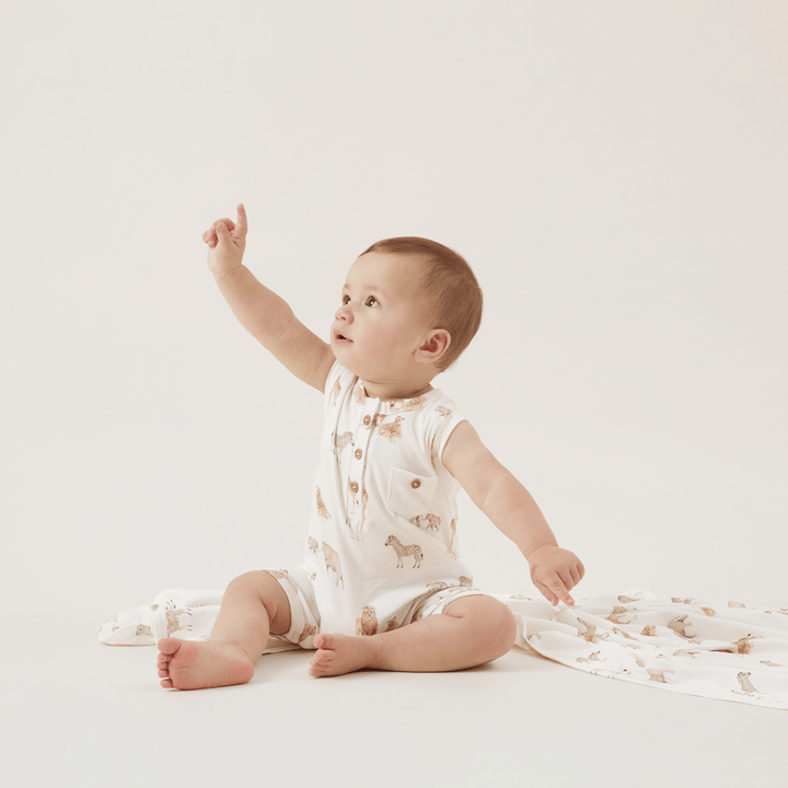 A baby is wrapped in an Aster & Oak Organic Cotton Baby Swaddle Wrap, surrounded by a teddy bear, against a white background.