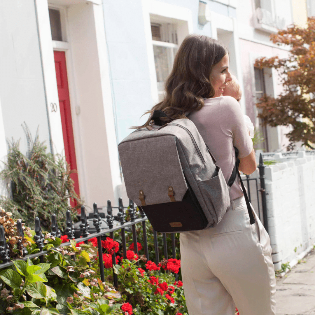 Smiling-Woman-By-Flowers-Holding-Baby-Wearing-Babymel-George-Eco-Nappy-Backpack-Naked-Baby-Eco-Boutique