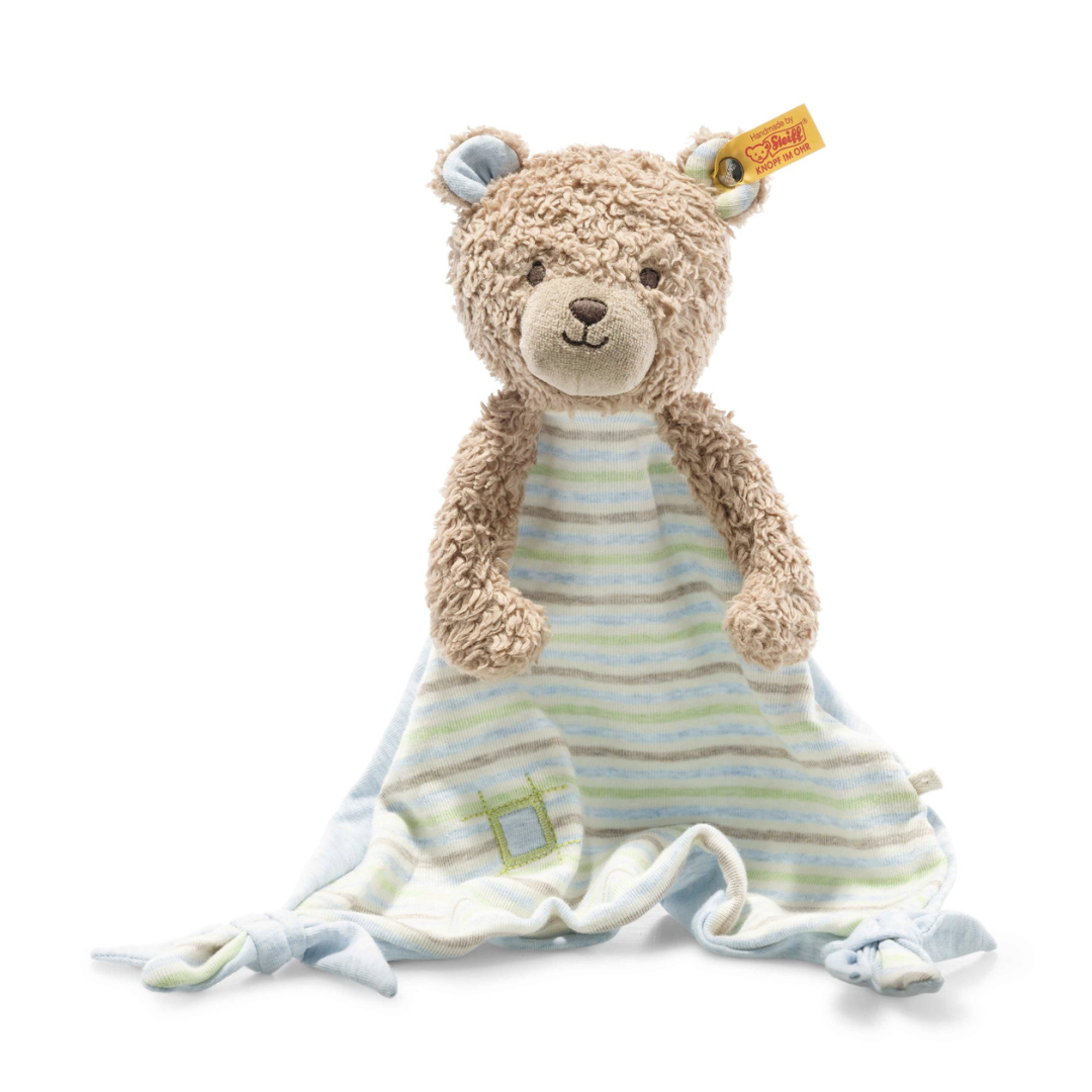 A Steiff Organic Teddy Bear Comforter with a tan head and arms, wearing a light blue and white striped blanket. The blanket, made from organic cotton wool, features green accents and a small green square patch near the bottom. This adorable toy is part of the GOTS line by Steiff, ensuring it meets high organic standards.