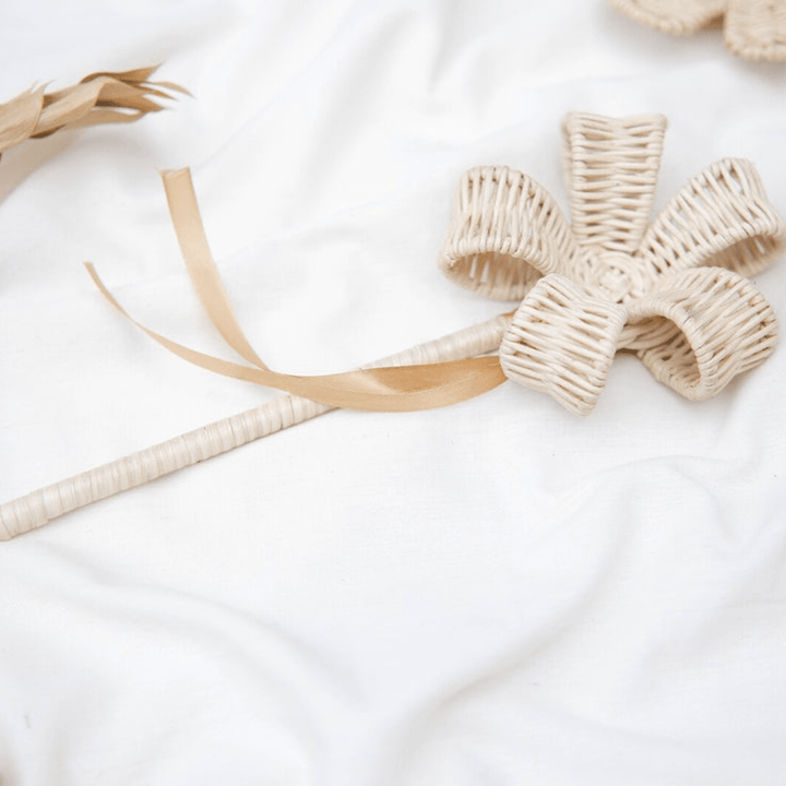 Lovingly crafted, the Classical Child Rattan Flower Wand from The Woodlands showcases a looped bow design and a delicate ribbon on a white cloth background, making it ideal for imaginative play.