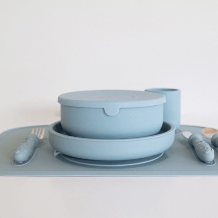 Introducing the Zazi Clever Mat, a blue, minimalist dinner set by Zazi that includes a lidded bowl, plate, cup, fork, and spoon—all crafted with food-grade silicone for safety and durability. The set comes perfectly coordinated on a matching blue Clever Mat.